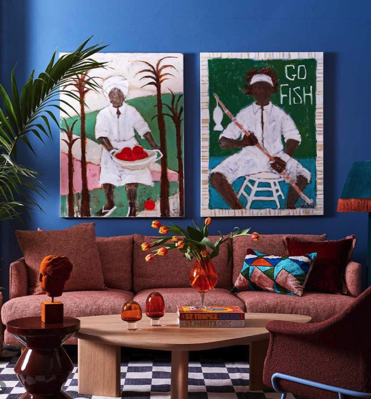 Two bold figurative paintings on a deep blue wall above a red sofa, The Style Workshop