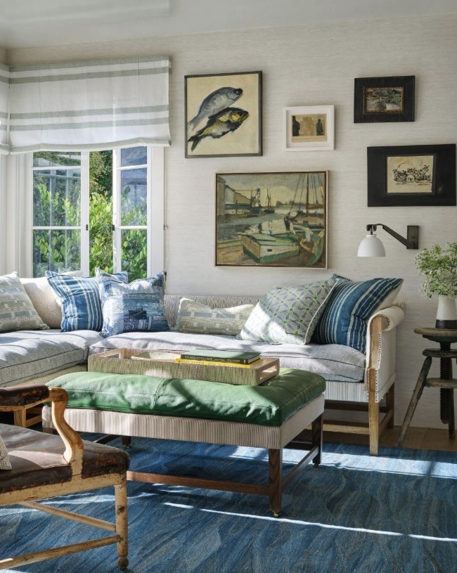 Living room with a collection of paintings and prints gathered above a sofa and around a window, The Style Workshop