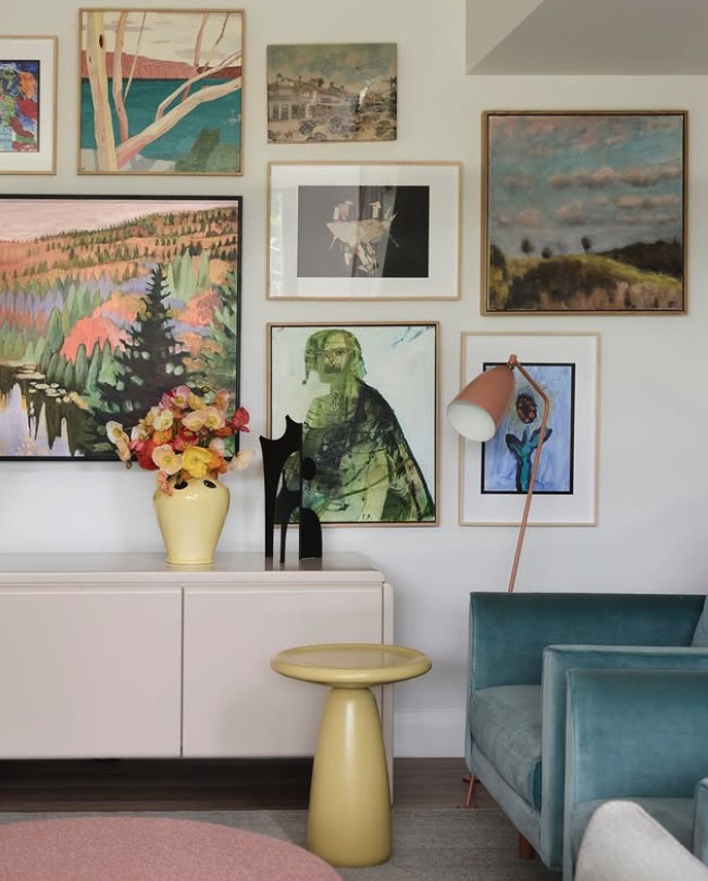 Gallery wall of landscape paintings and prints above a low cabinet, The Style Workshop