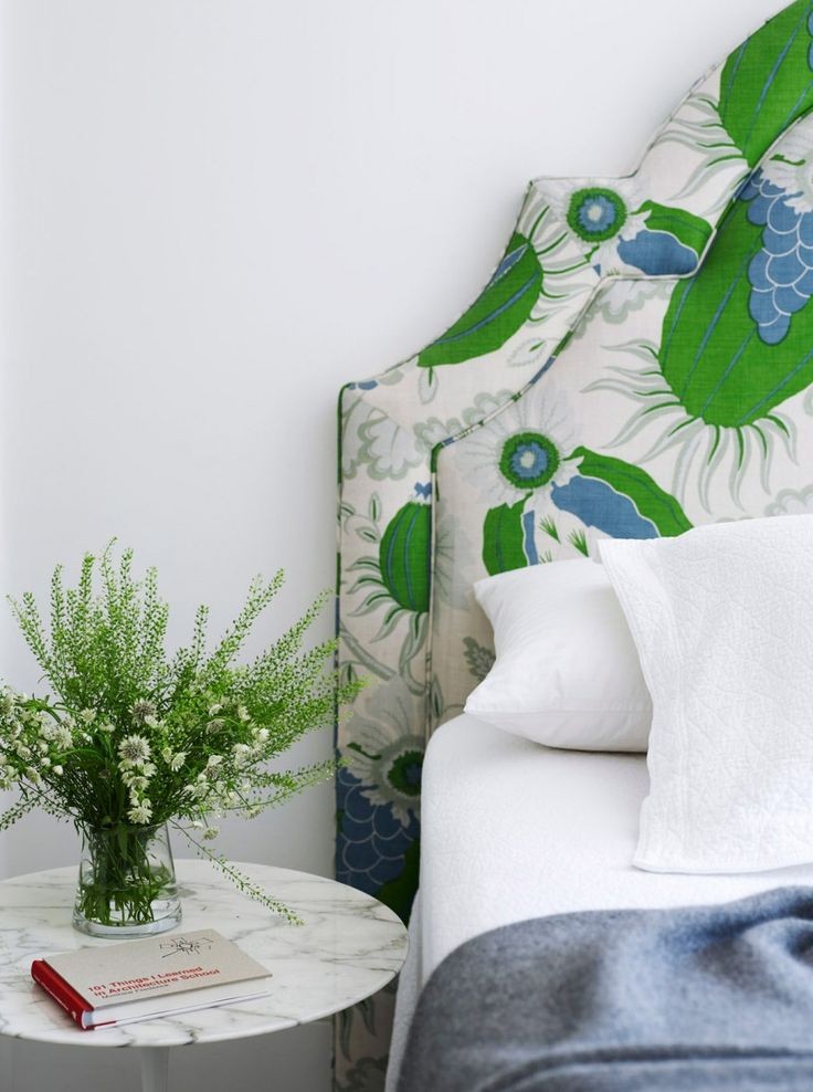 Bed with green and blue floral upholstered headboard, crisp white linen and wildflowers on a marble side table, The Style Workshop