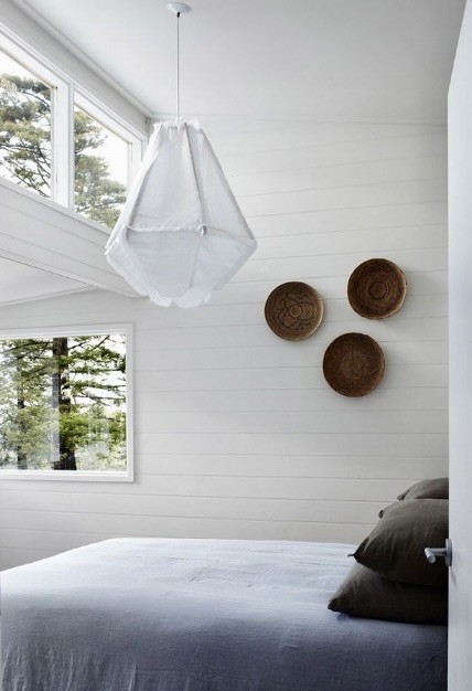 All-white bedroom with woven baskets on the wall and pale linen bedding, The Style Workshop