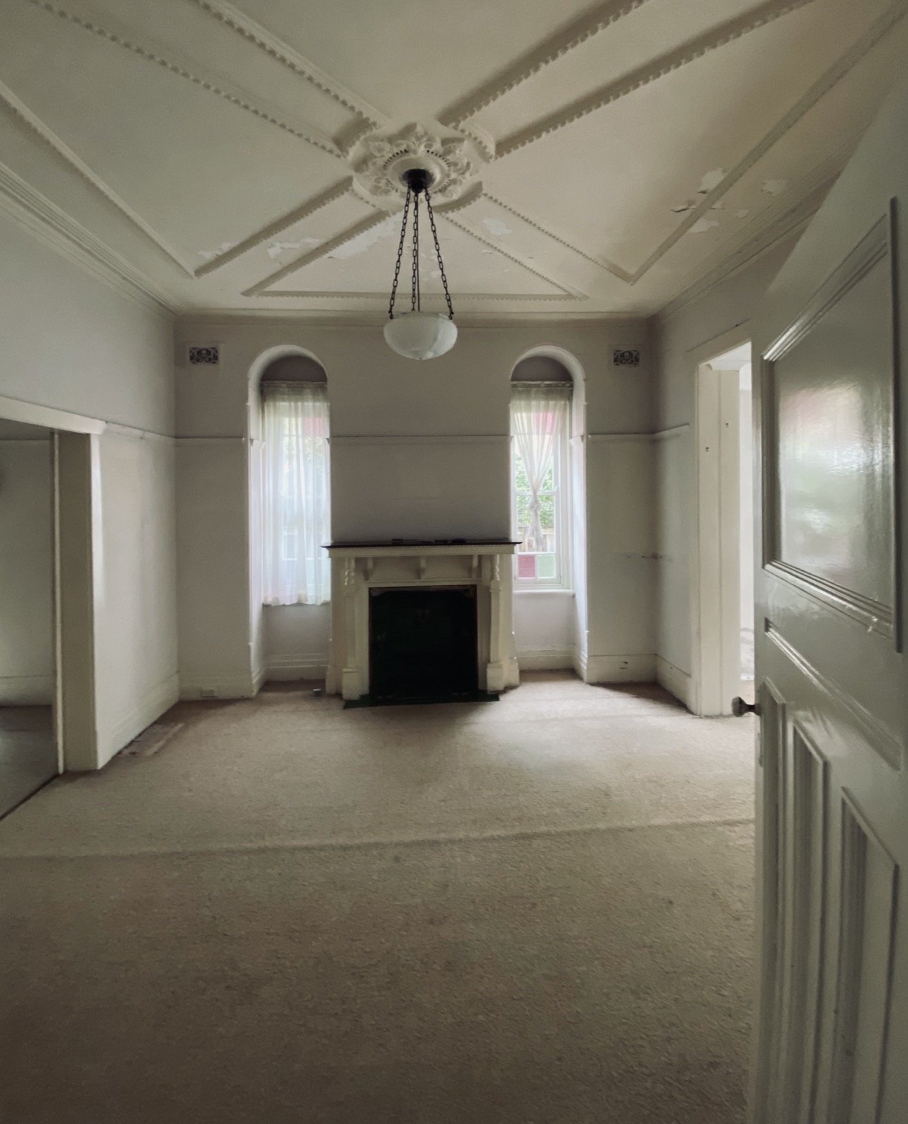 Original Federation sitting room before renovation, with fireplace, ornate ceiling detail and arched leadlight windows
