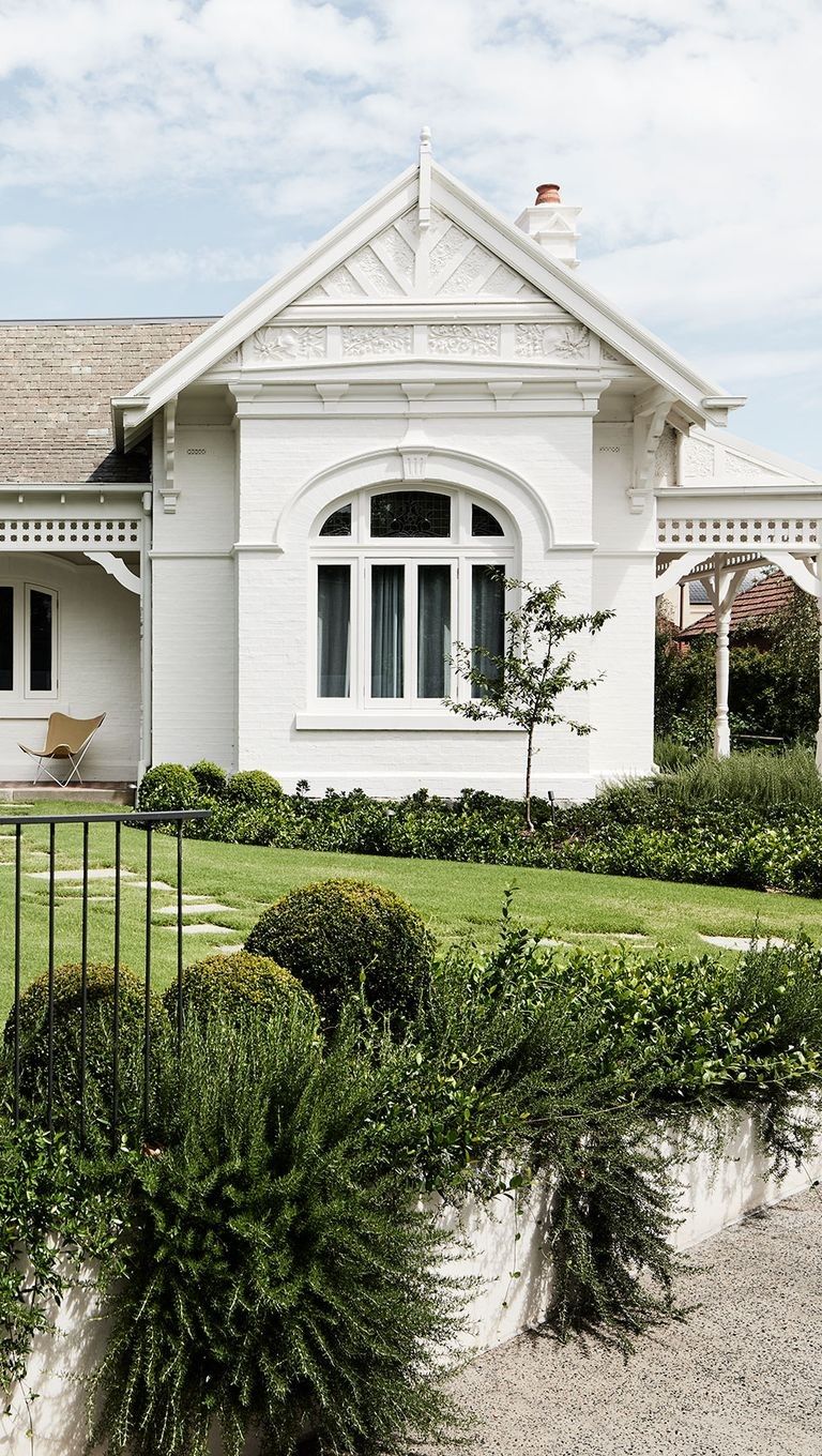 Painted white Federation home facade with ornate gable pediment detail, arched leadlight window and return verandah