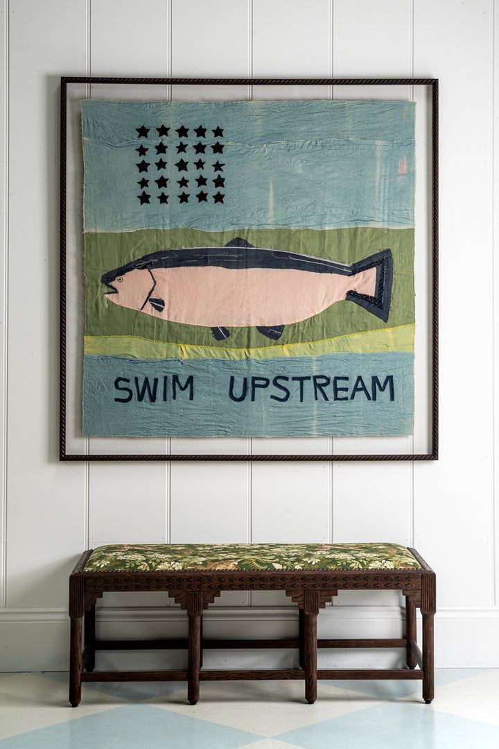Large hand-worked textile artwork above an antique carved bench