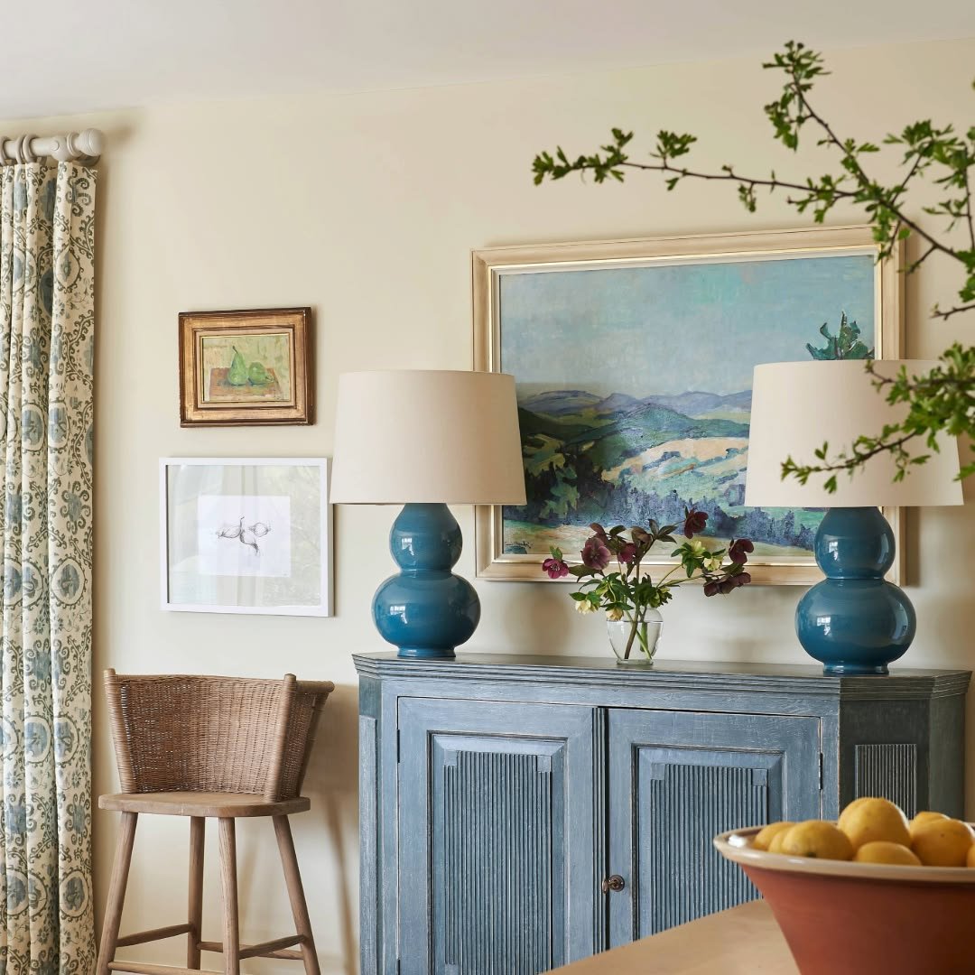 Pair of teal gourd lamps with cream shades on a blue painted console beneath a landscape painting