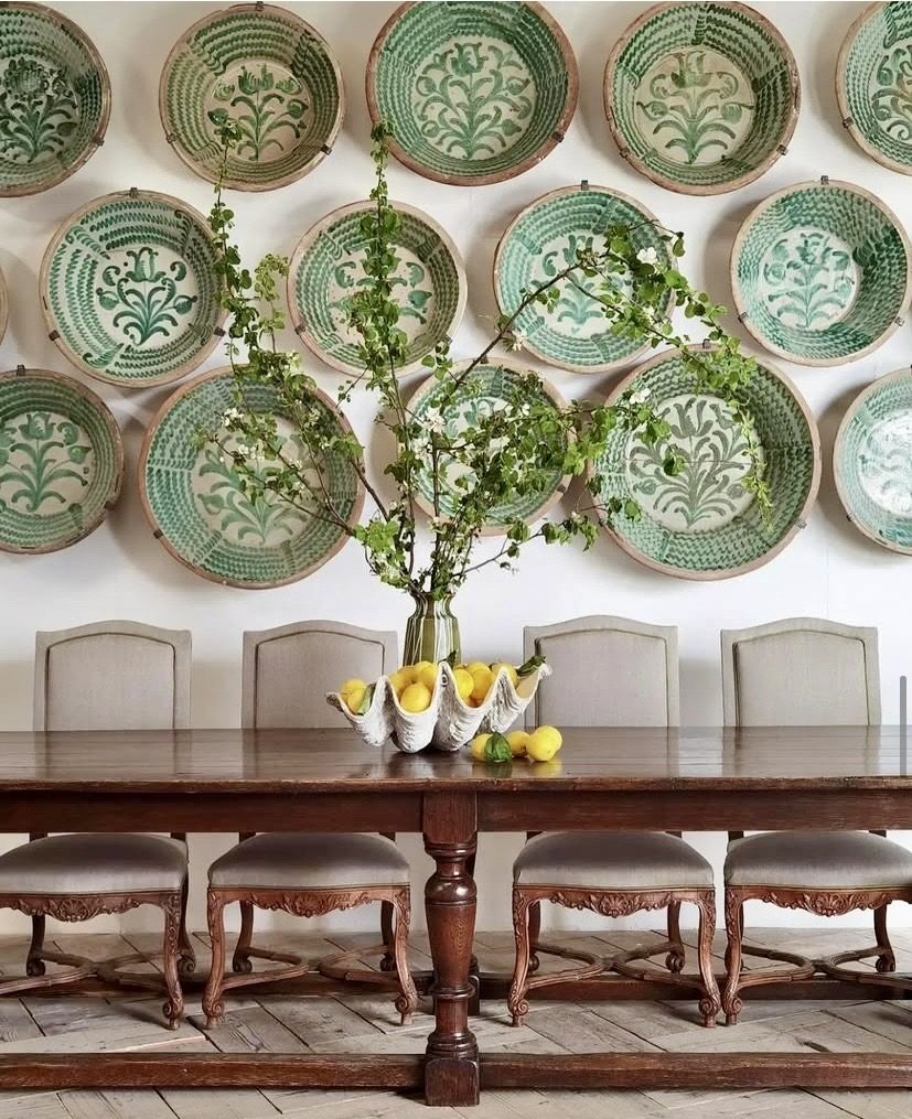 Wall of antique green and white platters above a rustic timber dining table, The Style Workshop