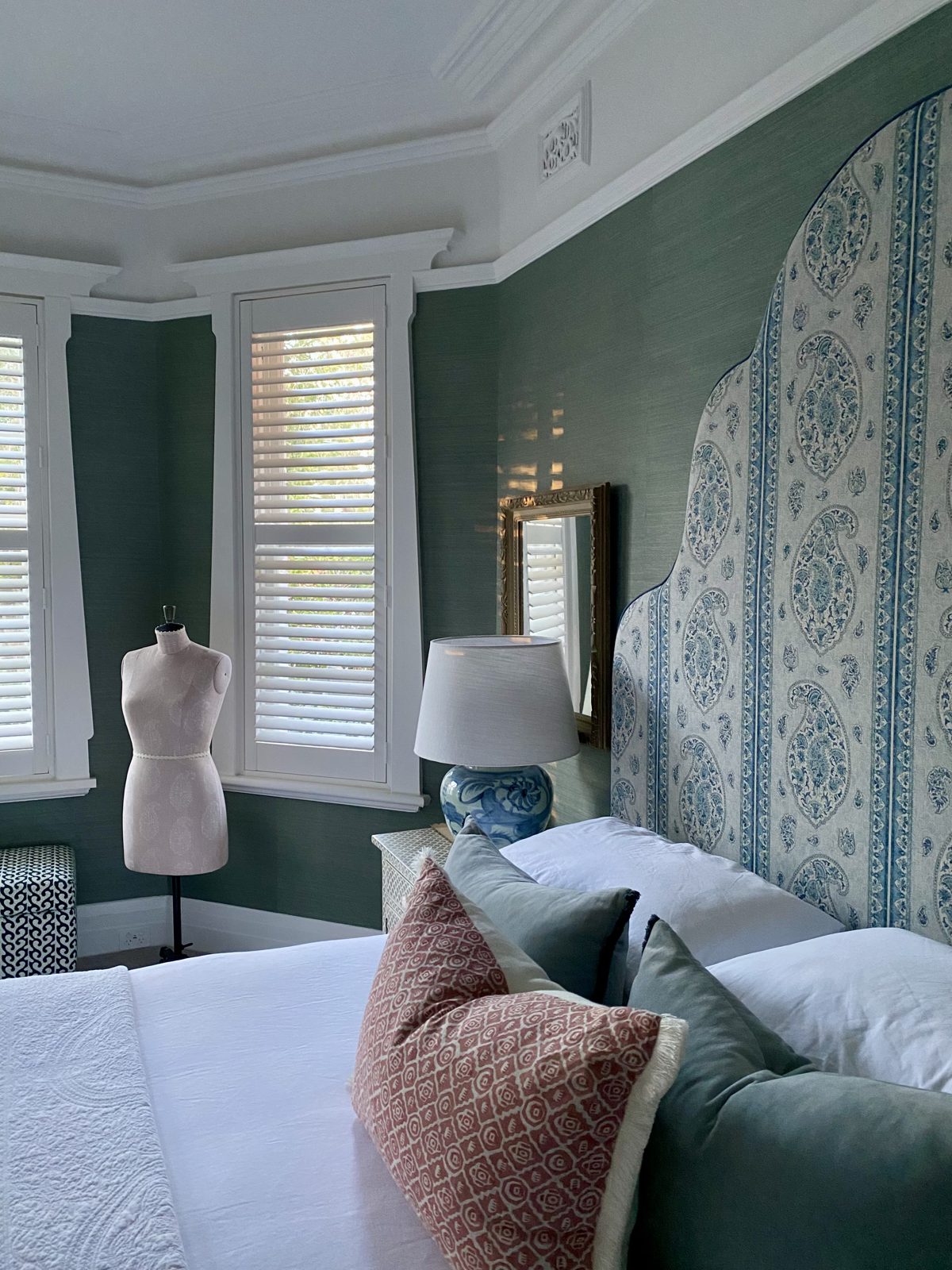 Bedroom with a vintage dress form, upholstered bedhead and green grasscloth walls, The Style Workshop
