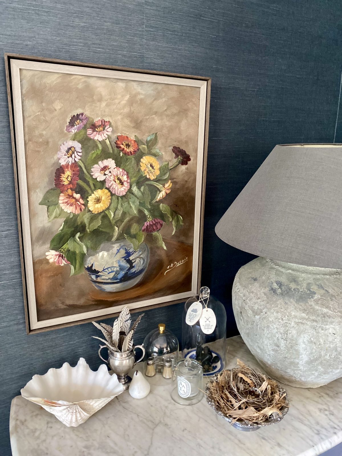 Vintage floral oil painting leaning on a marble console with a large stone lamp, The Style Workshop