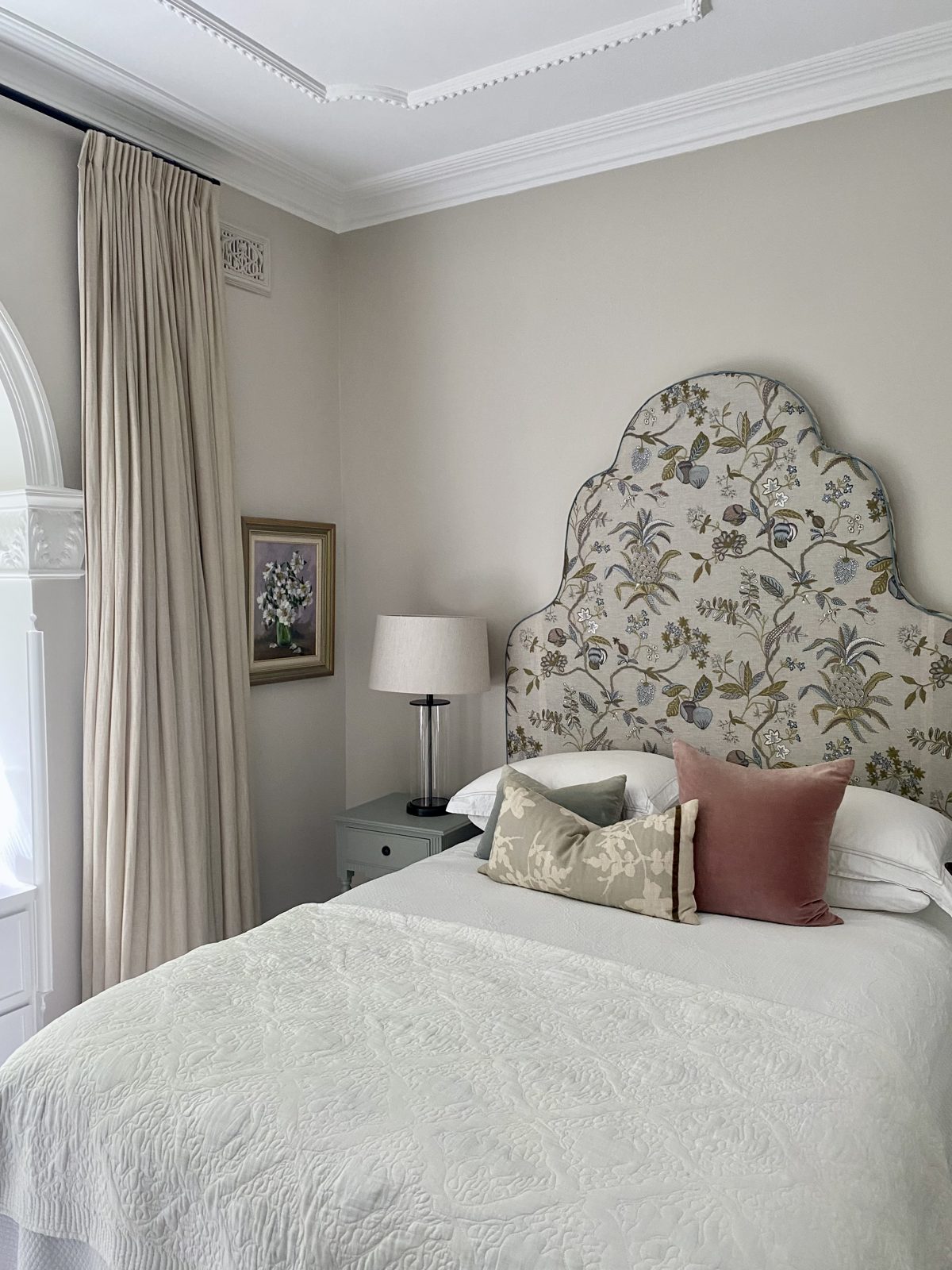 Light bedroom with a small vintage floral painting beside a floral upholstered bedhead, The Style Workshop