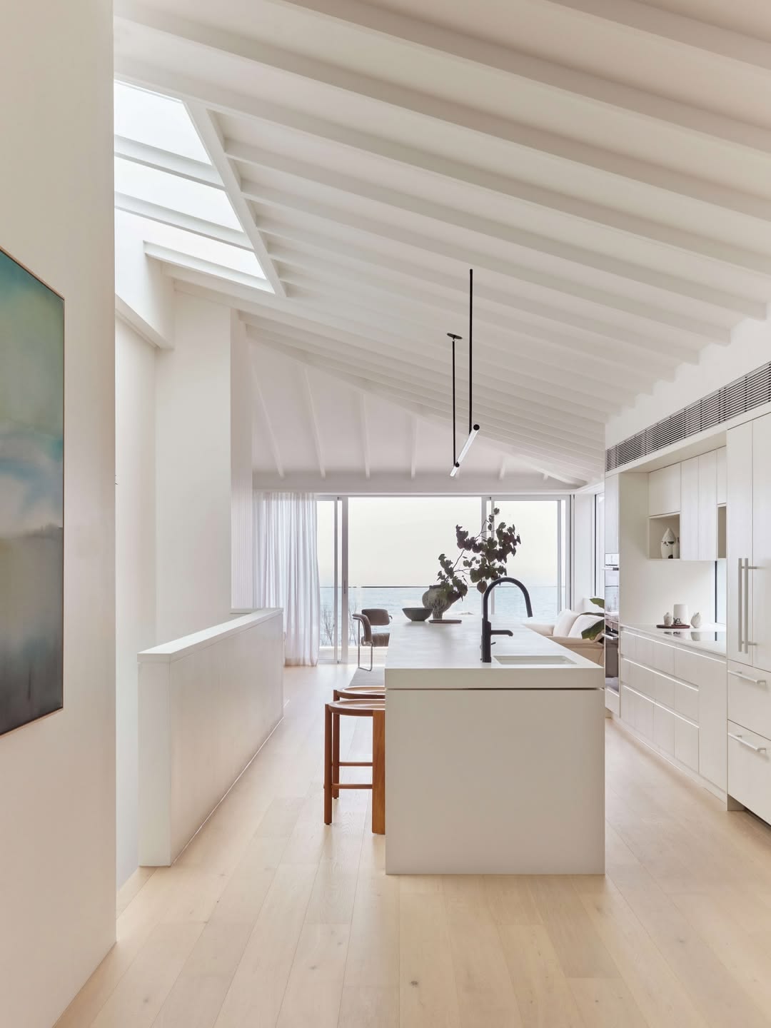 Contemporary coastal kitchen with white rafter ceiling, white island bench and ocean view