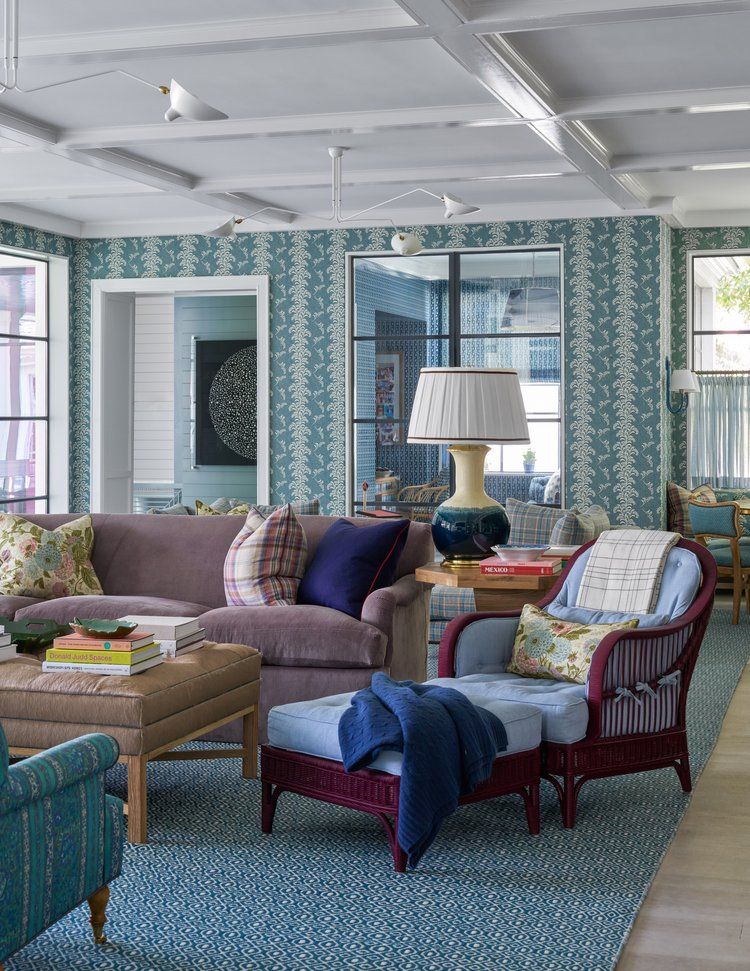 Living room with blue palm print wallpaper, patterned pillows and striped rattan chairs