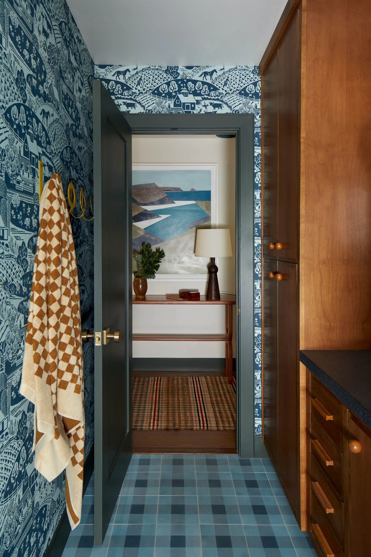 Mudroom with navy pictorial wallpaper and a checked towel on brass hooks