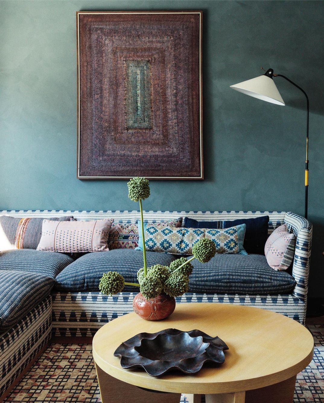 Deep teal living room with heavily patterned sofa and layered cushions