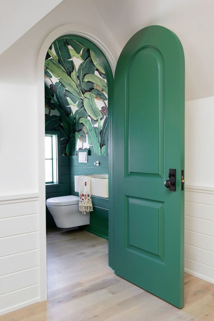 Green banana leaf wallpaper powder room behind an emerald door