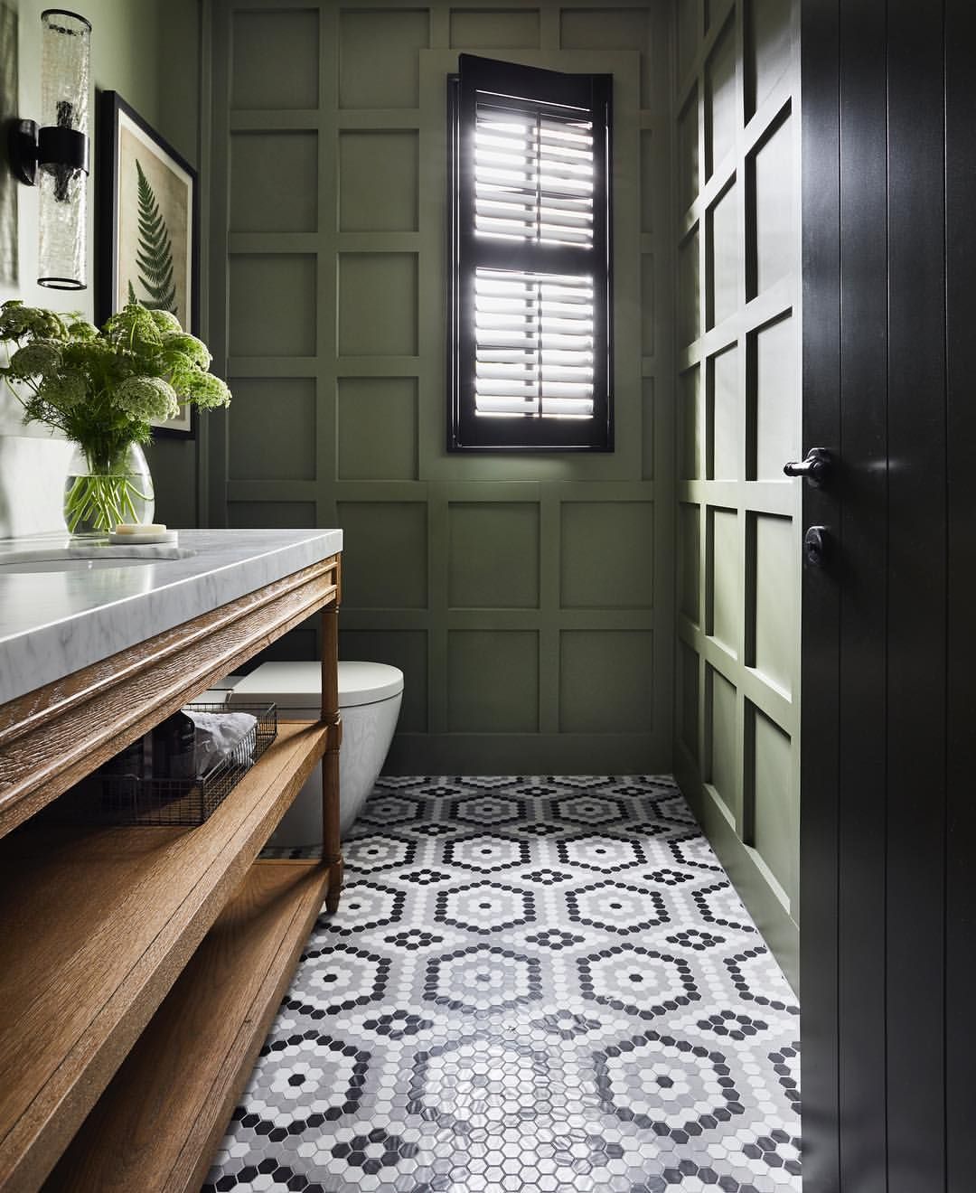 Olive green panelled powder room with black shutters and hexagon tile floor