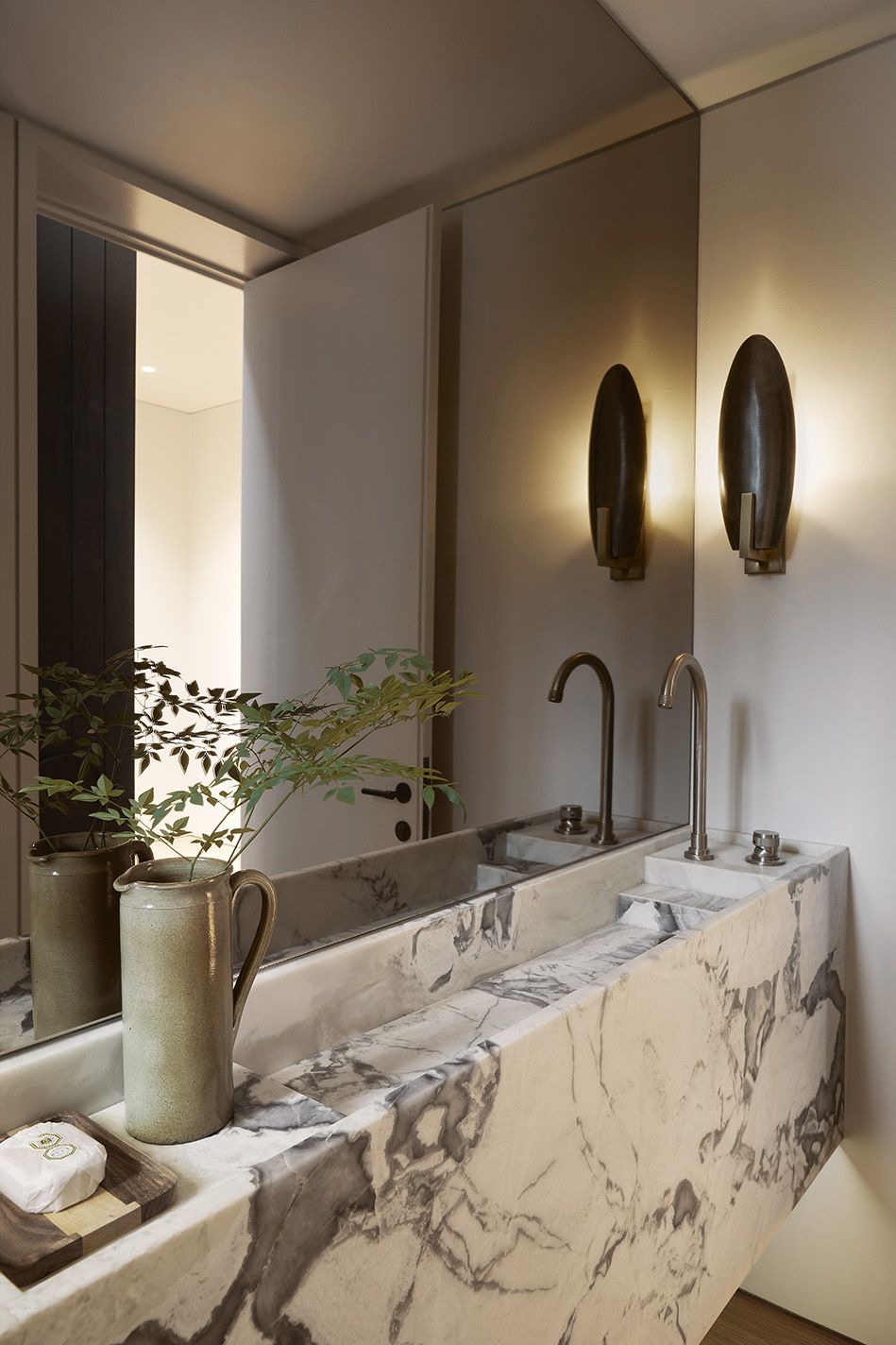 Sculpted marble trough vanity with brass tapware and bronze wall sconces