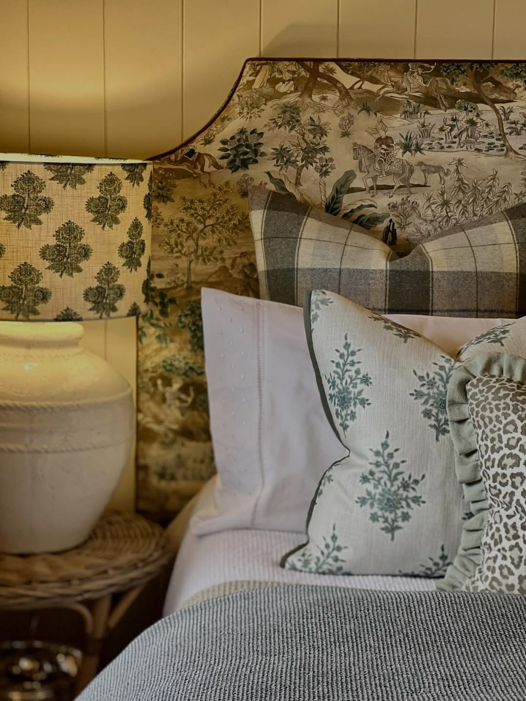 A considered bedroom vignette — upholstered bedhead, layered cushions and warm lamplight